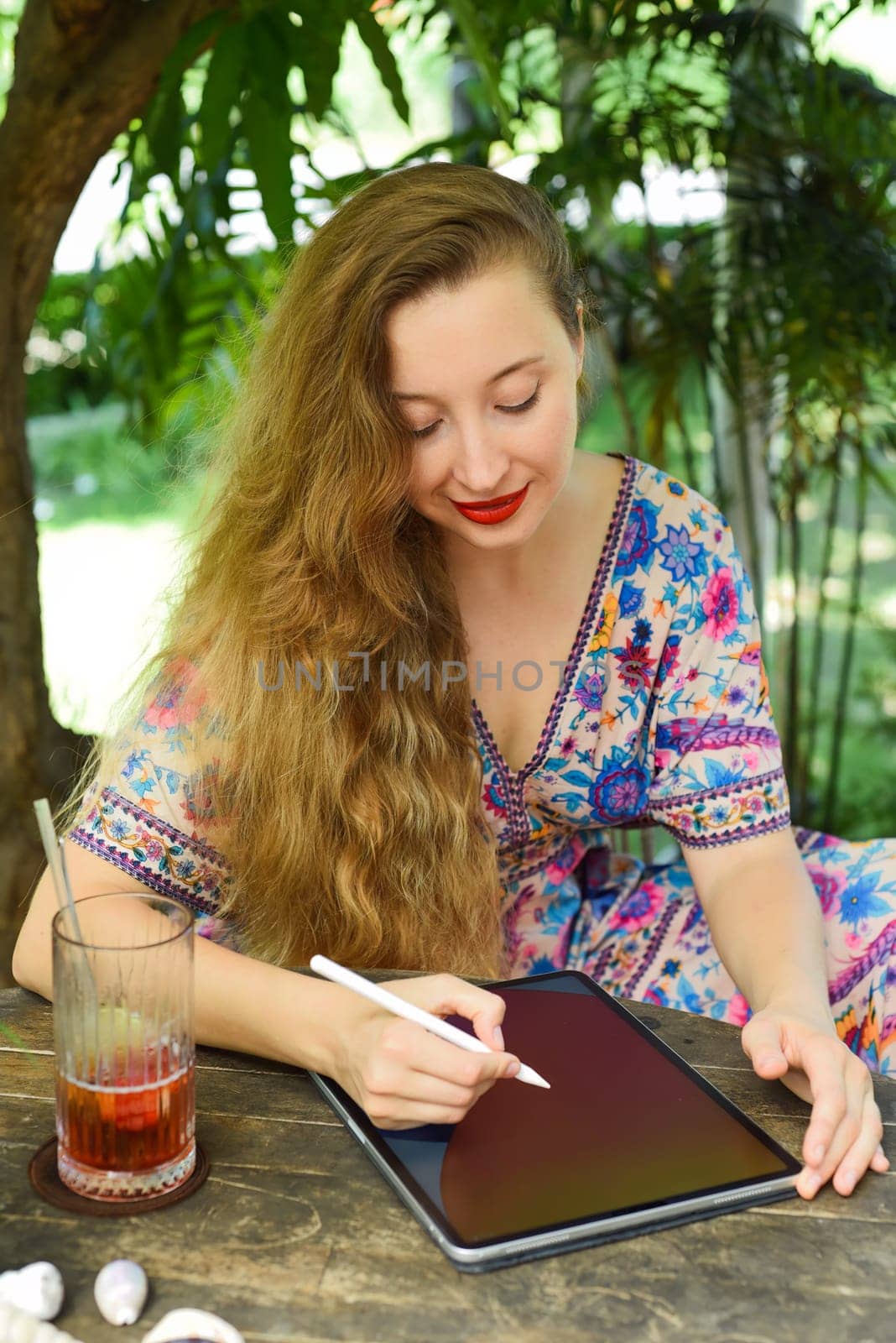 Beautiful blonde woman artist and illustrator drawing, sitting by the table with electronical tablet and stylus