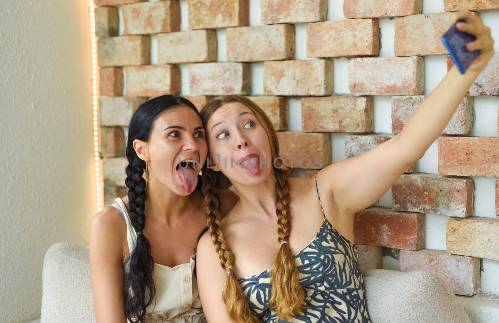 Ukrainian woman (brunette) and Russian woman (blonde) portrait together with braids posing and taking a selfie, showing tongue