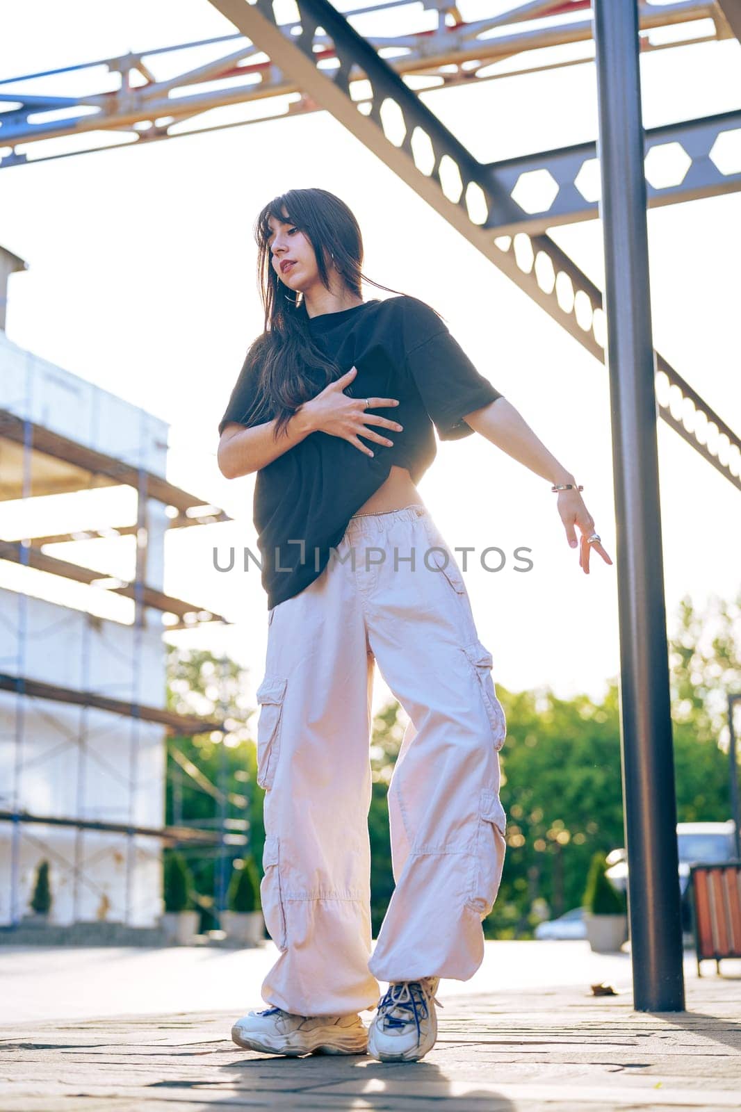 A dancer performs gracefully in a relaxed outfit as the sun sets behind a construction area, creating a vibrant and dynamic atmosphere filled with energy.