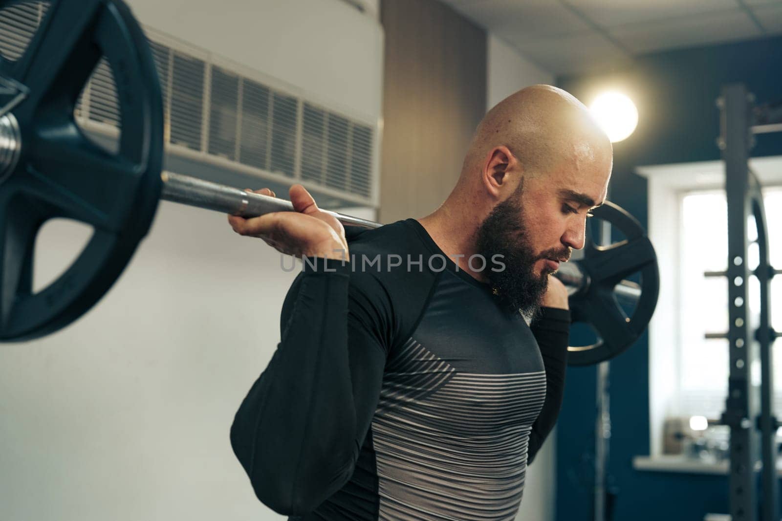 A male athlete engages in a weightlifting routine, performing a squat with a loaded barbell at a well-equipped gym. The atmosphere is motivated and intense.