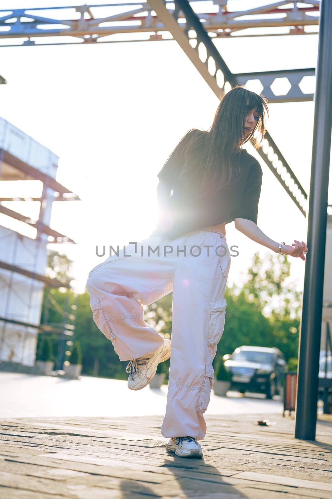 A young woman performs a dance move outdoors at sunset, surrounded by early construction. The warm light creates a captivating atmosphere as she enjoys her moment.