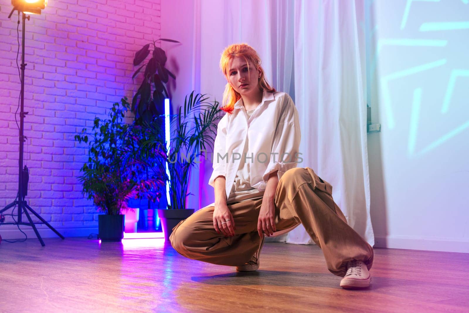 A dancer showcases her skills in a vibrant studio filled with colorful lights and plants. The atmosphere is energetic, highlighting her dedication to dance during evening hours.