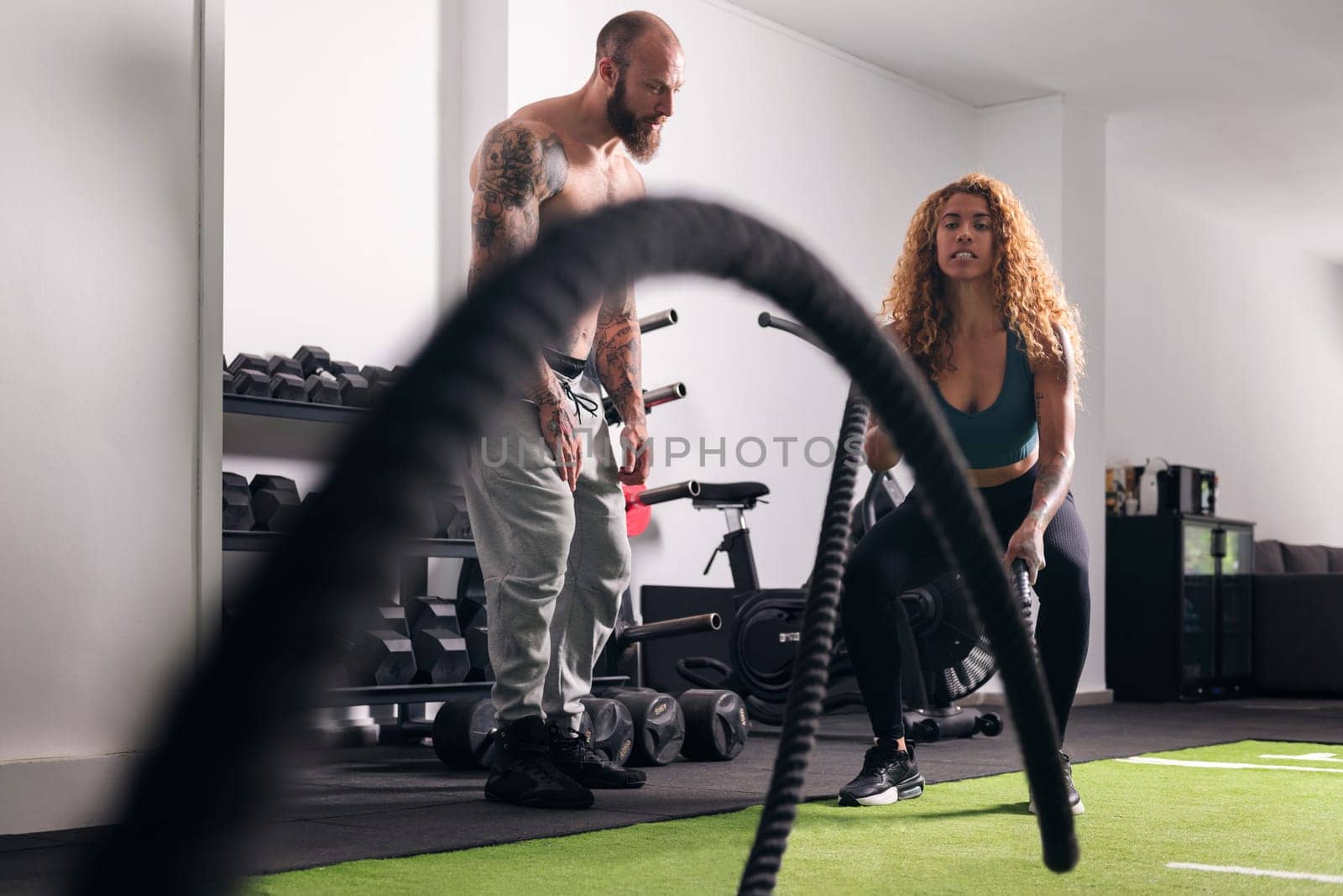 muscular sportswoman doing exercise with rope during functional workout with male buddy at gym, concept of fitness and active lifestyle