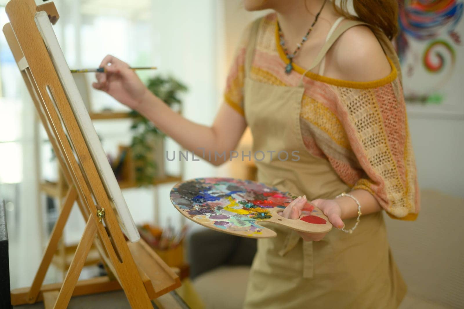 Cropped shot of artist holding palette while creating artwork on a canvas.