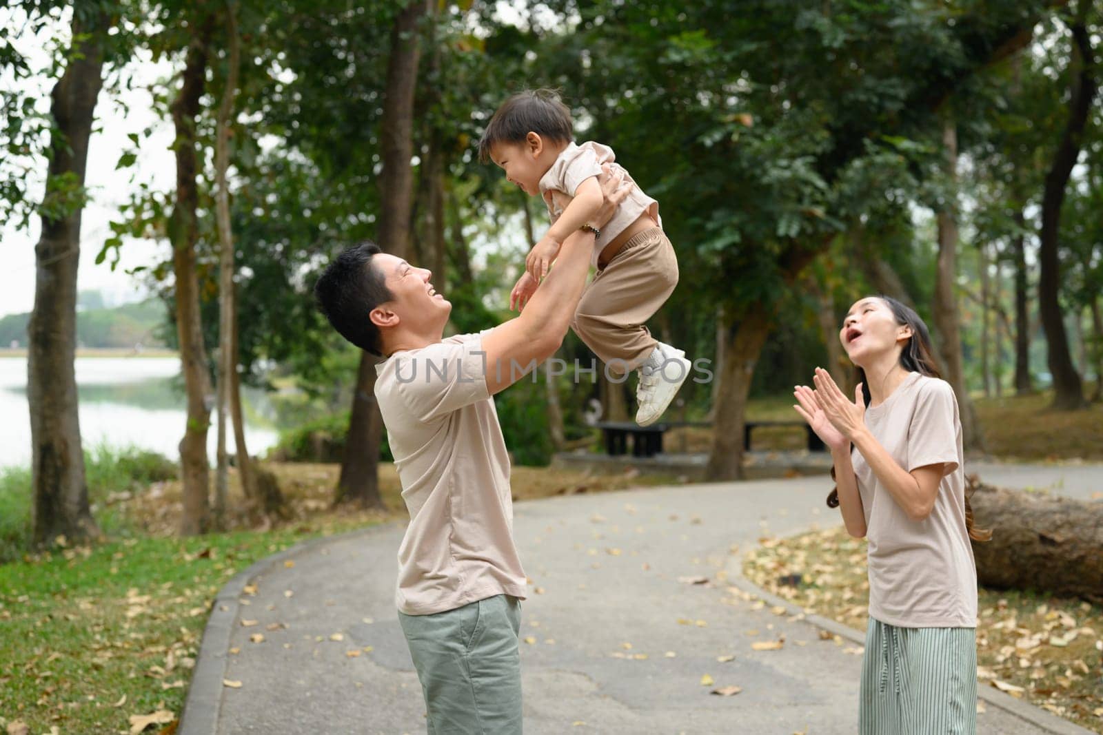Cheerful parents and their sons having fun while walking in beautiful green park.