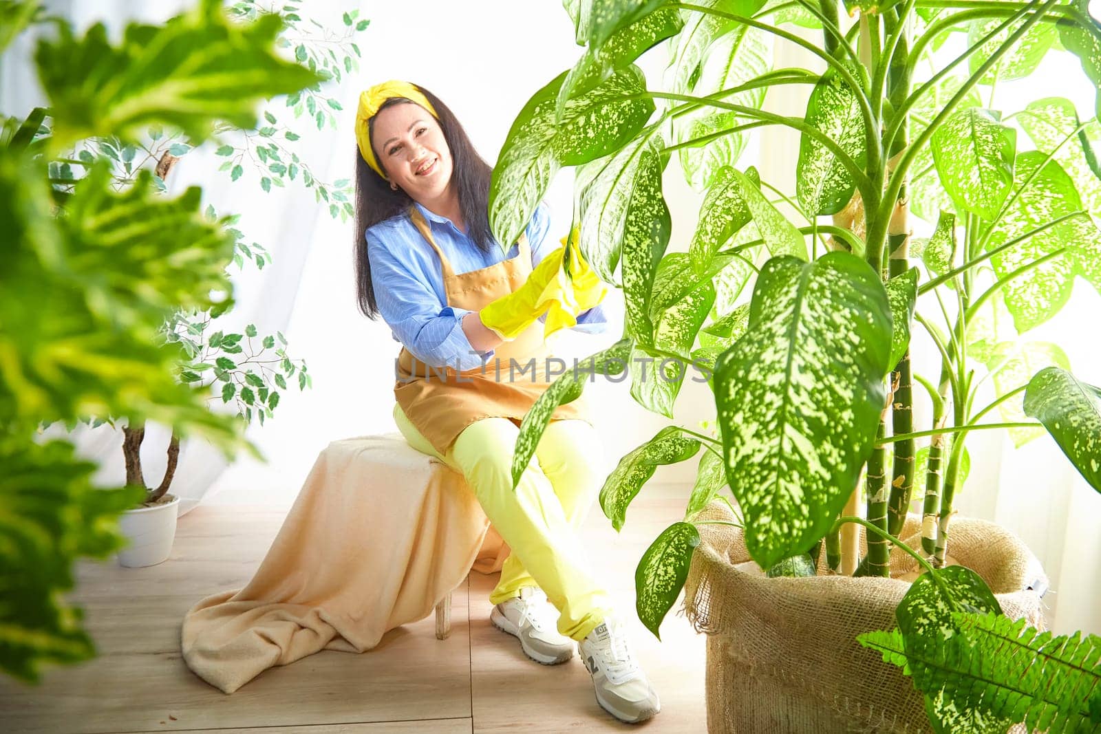 The gardener smiles while caring for thriving plants in a bright, cheerful greenhouse.