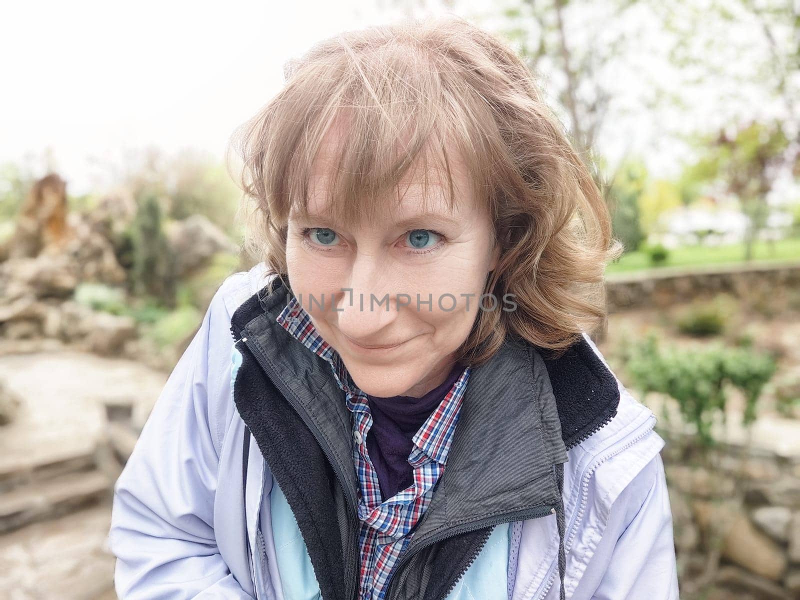 A middle-aged woman playfully takes selfies while exploring a lovely park during her trip, enjoying the natural surroundings.