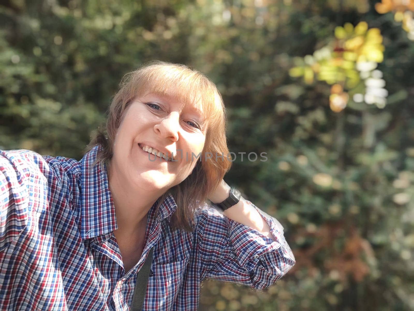 Blonde woman captures her joyful moment in a nature setting during her autumn journey, surrounded by colorful foliage.