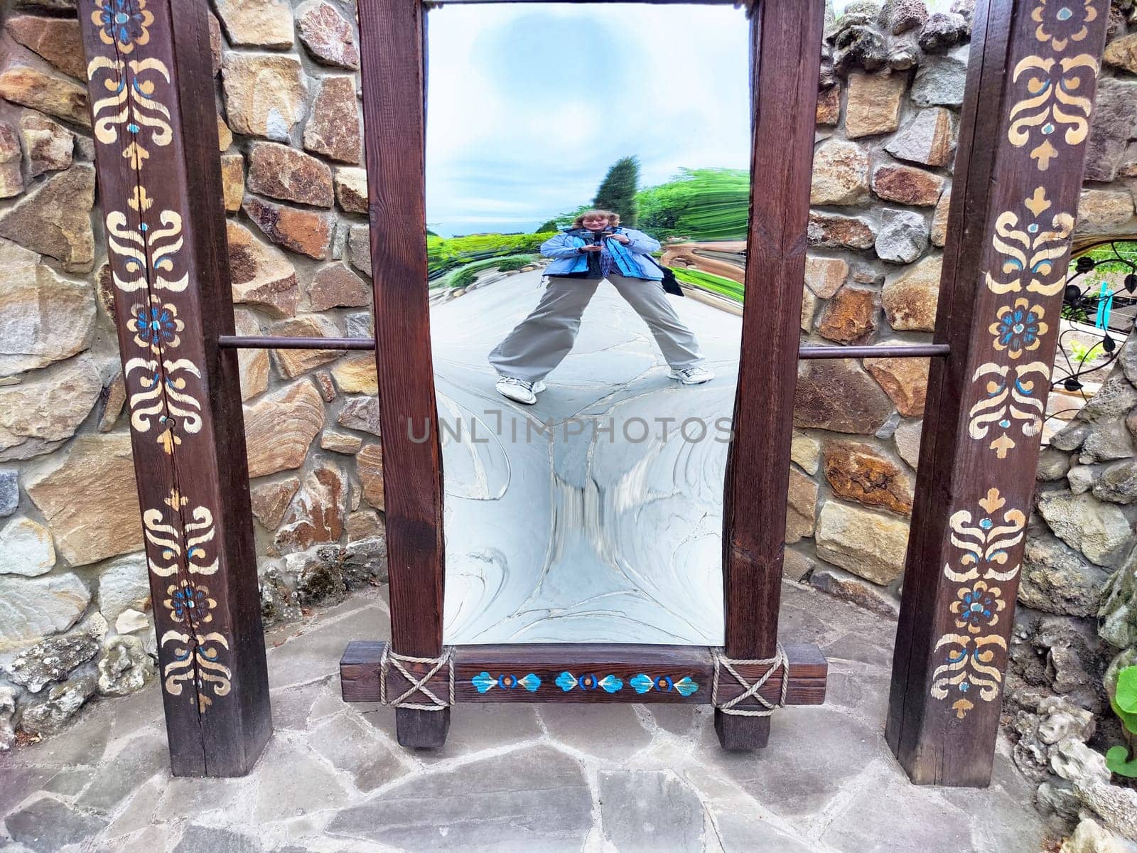 A modern, middle-aged woman playfully poses for a funny selfie in a curved mirror while enjoying a park outing.