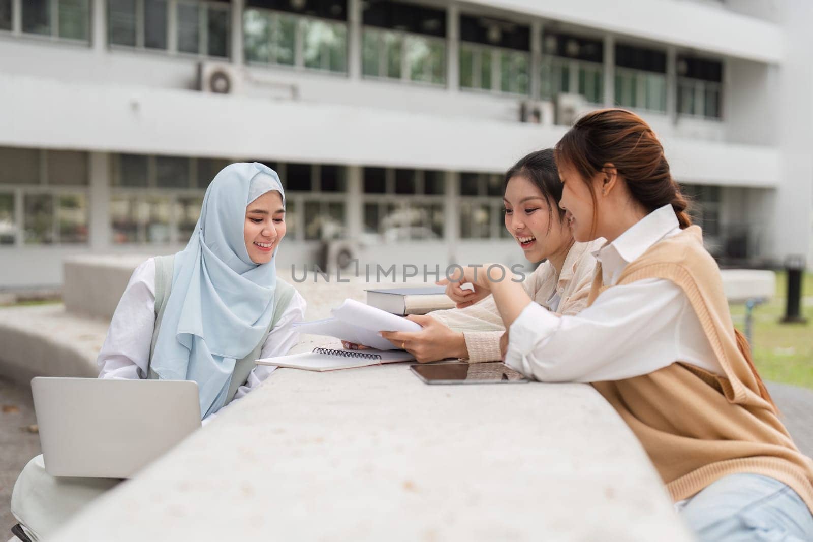 A group of diverse university students engaged in study sessions outdoors, sharing notes and discussing ideas at a campus table.