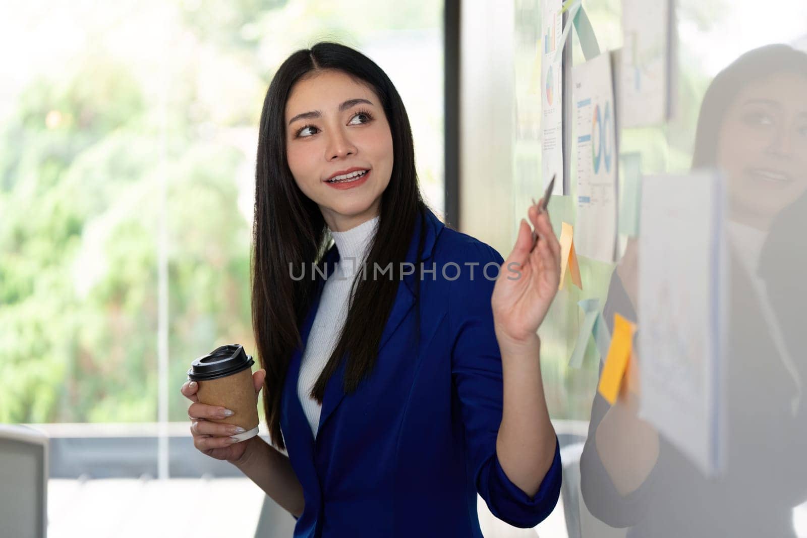 A diverse businesswoman engaging her team by presenting analysis findings on a whiteboard, promoting collaboration and effective communication in a modern office environment.