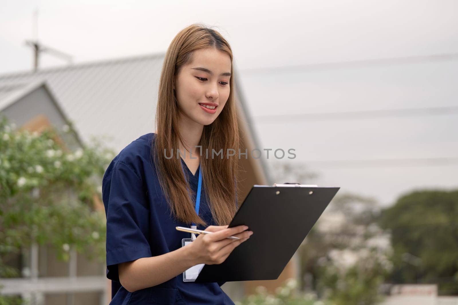 A smiling female healthcare professional in scrubs enjoys a moment of relaxation while reviewing notes outdoors, emphasizing the importance of balance in her role.
