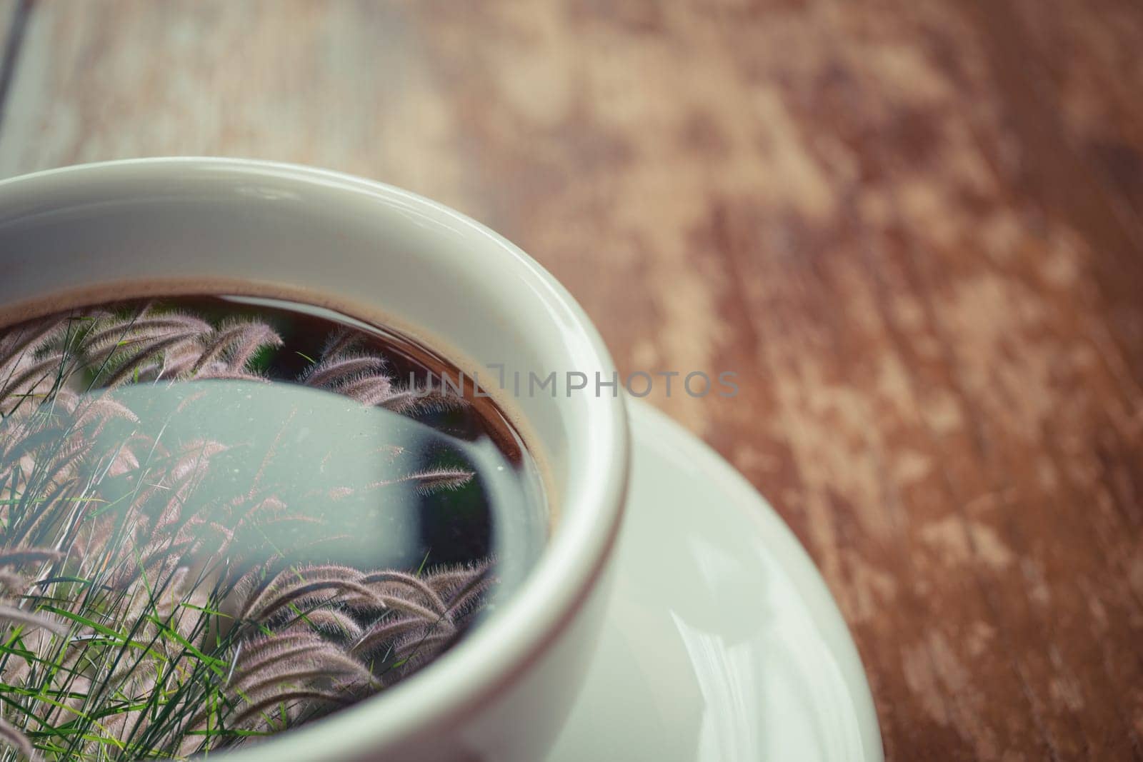 Grass flower (poaceae) reflection on Coffee in white cup on wood table , process in vintage style