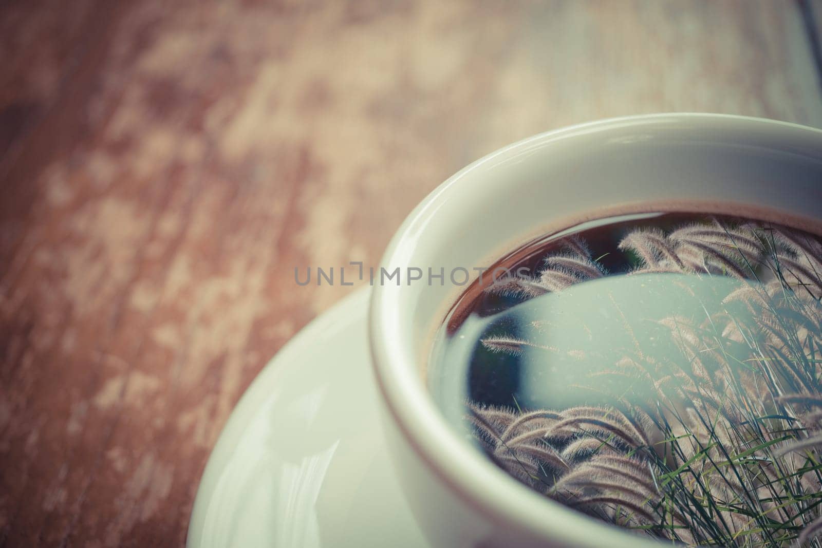 Grass flower (poaceae) reflection on Coffee in white cup on wood table , process in vintage style