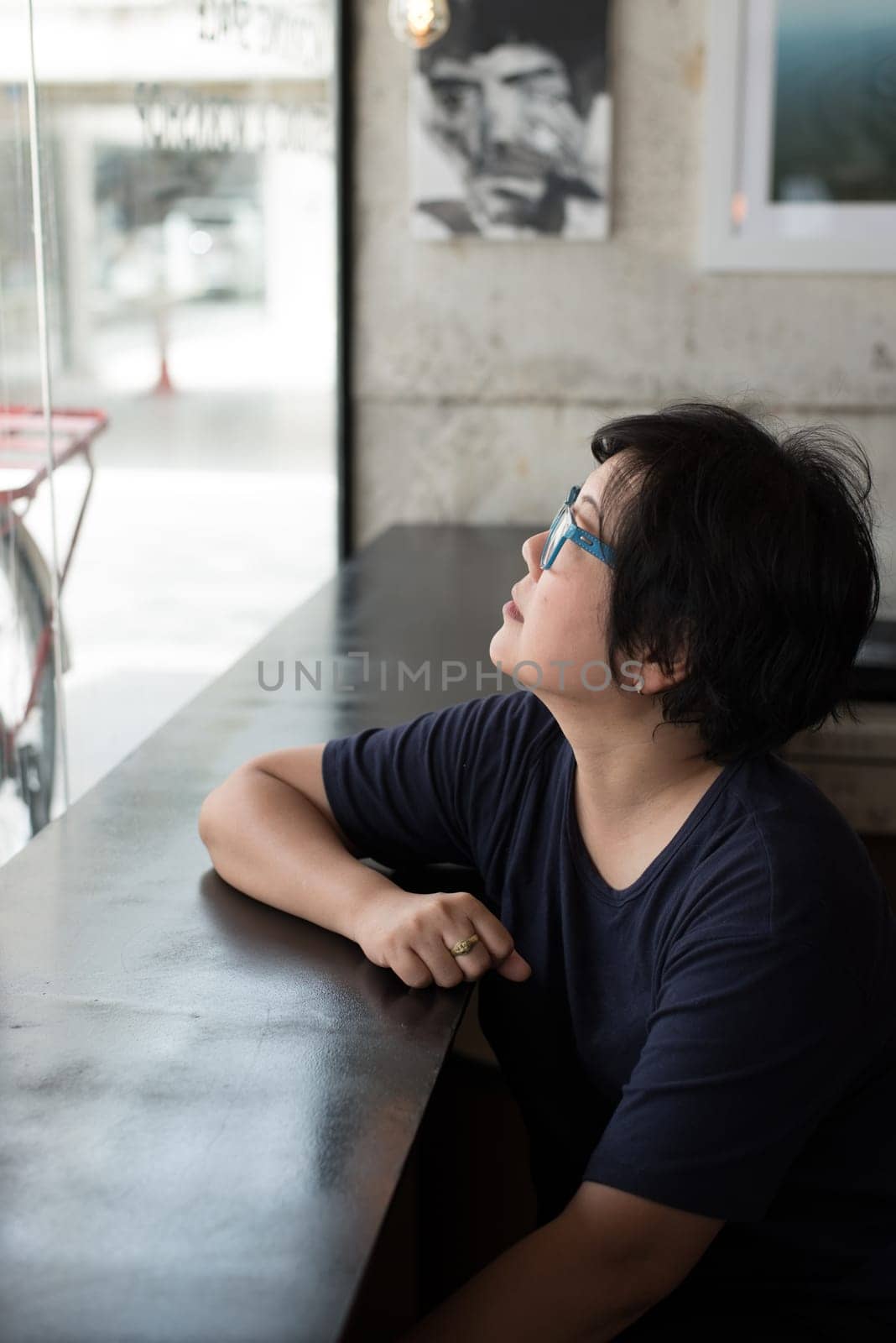Asian women 40s white skin in black dress with eye glasses have a doubt and think gesture in a coffee shop cafe