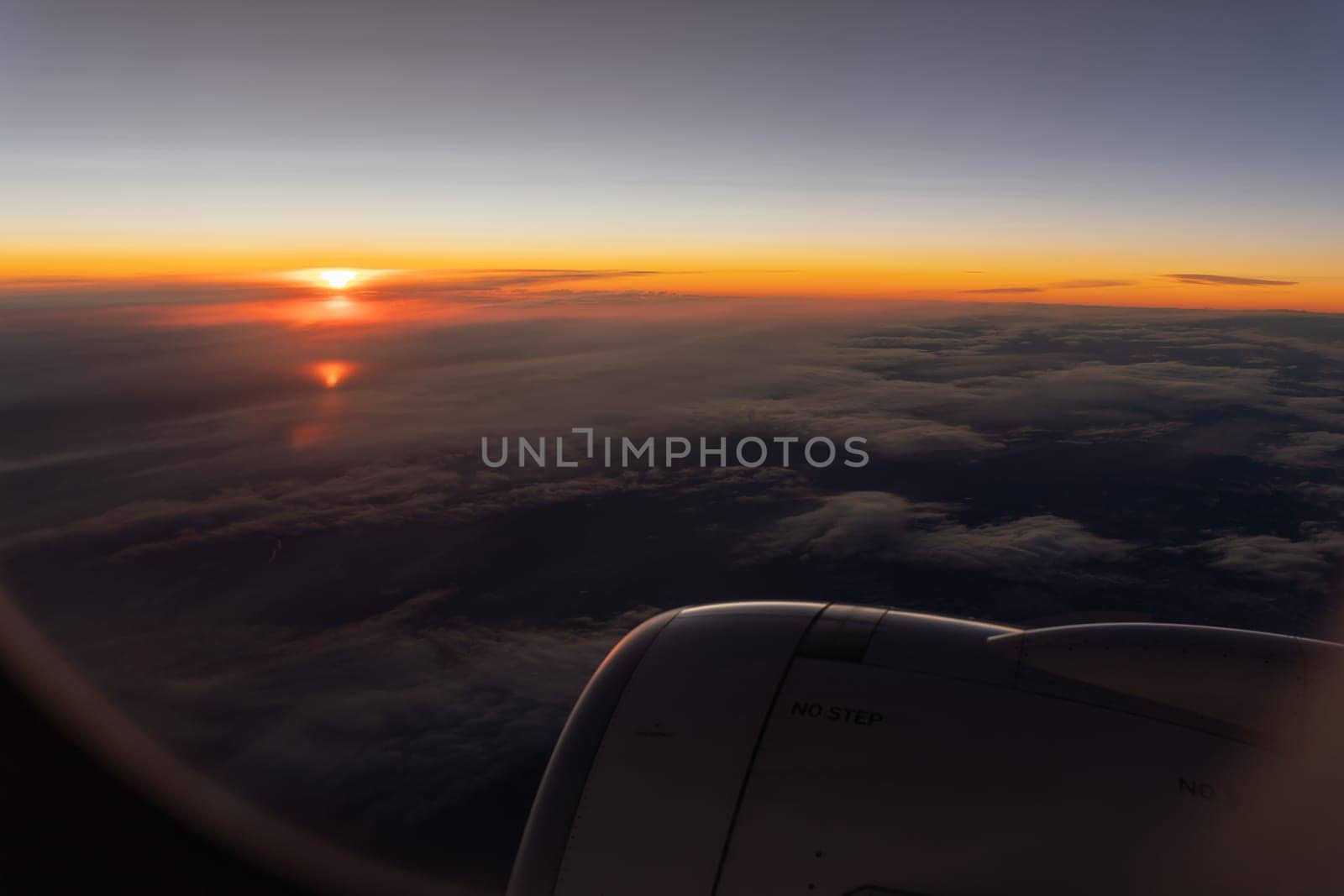 Bright orange sunrise on the horizon over grey clouds. Passenger POV from the plane