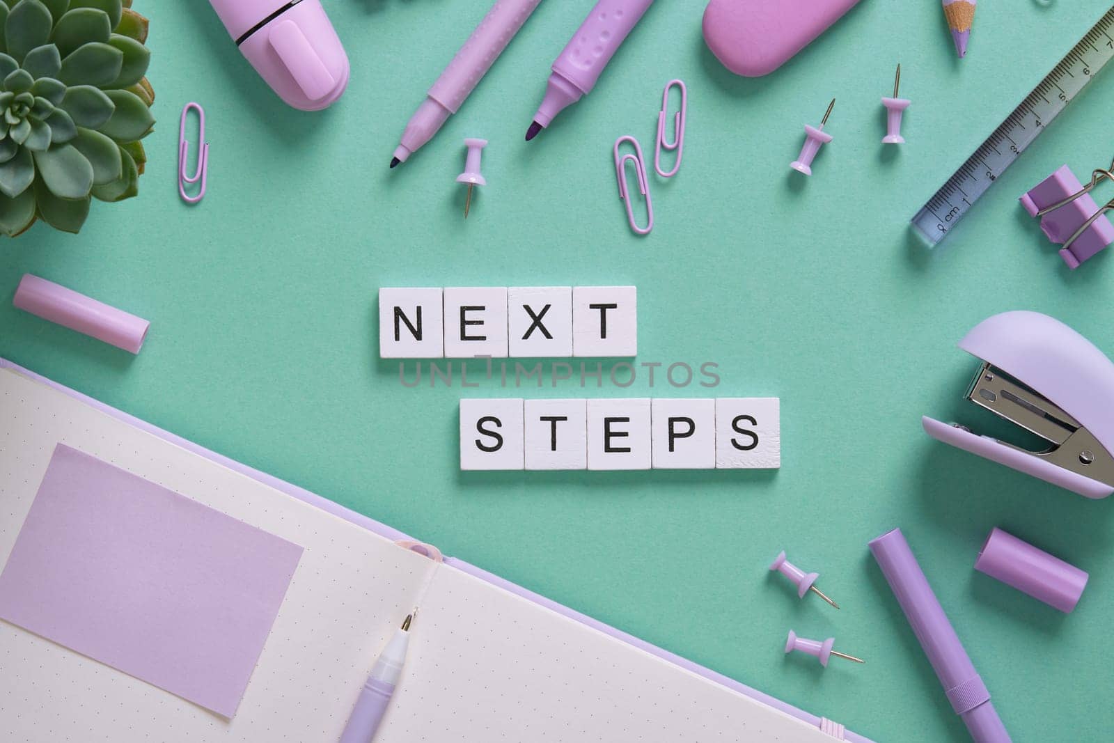 Words Nest Steps in English made of wooden blocks on a background of purple stationery. Mint green backdrop.