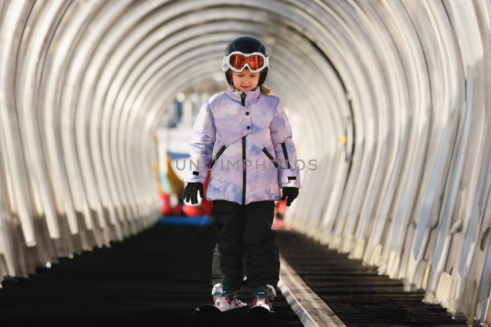 A girl on skis stands on a carpet ski lift in a tunnel