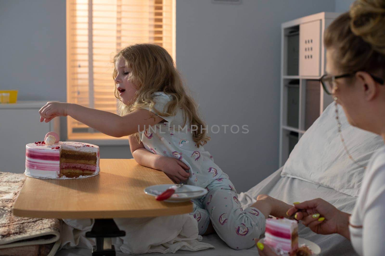In a cozy hospital environment, a child joyfully shares a delicious cake with a loving caregiver, creating warmth