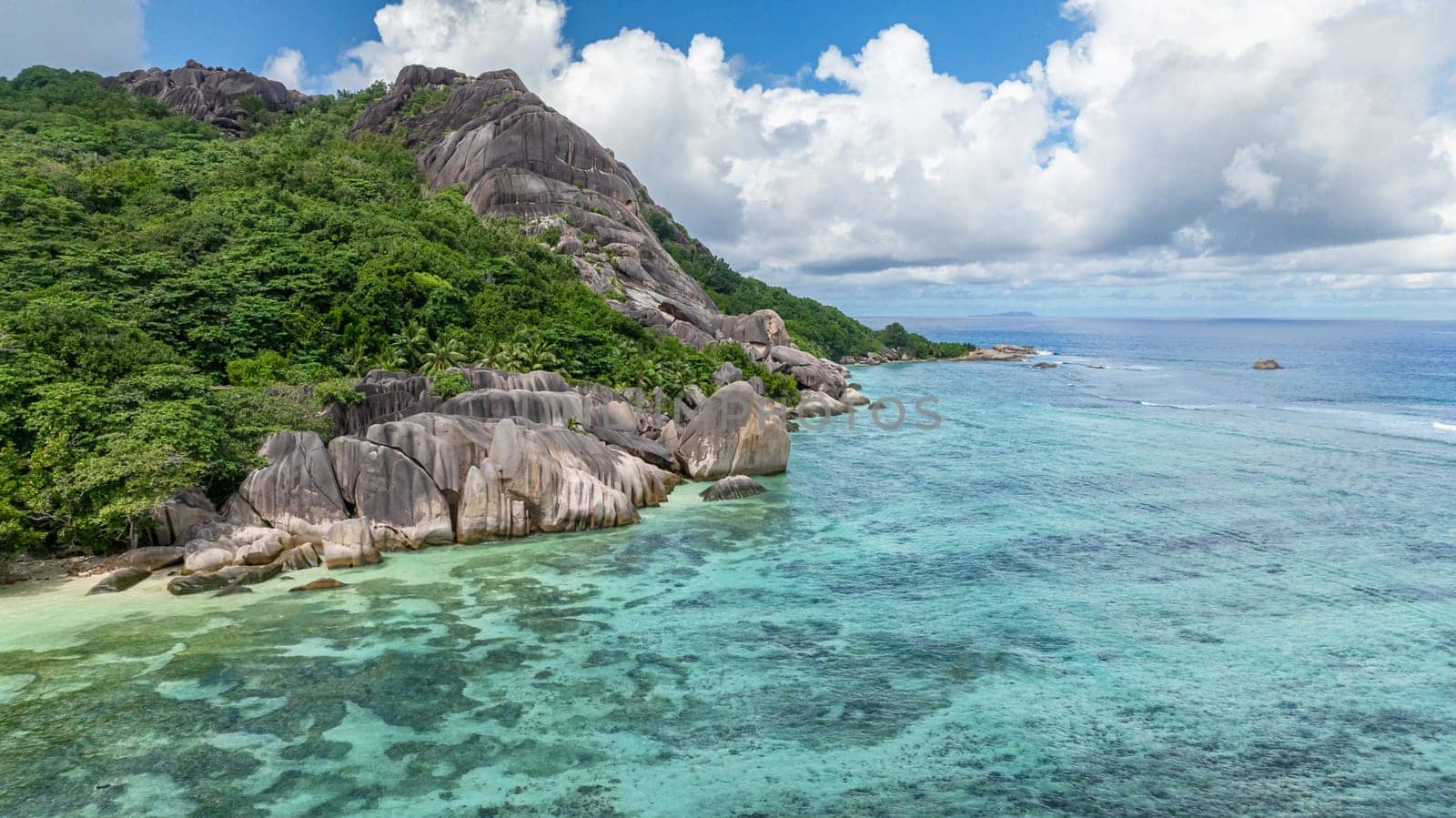 Large granite boulders meeting clear ocean waters along a scenic coastline. La Digue, Seychelles.