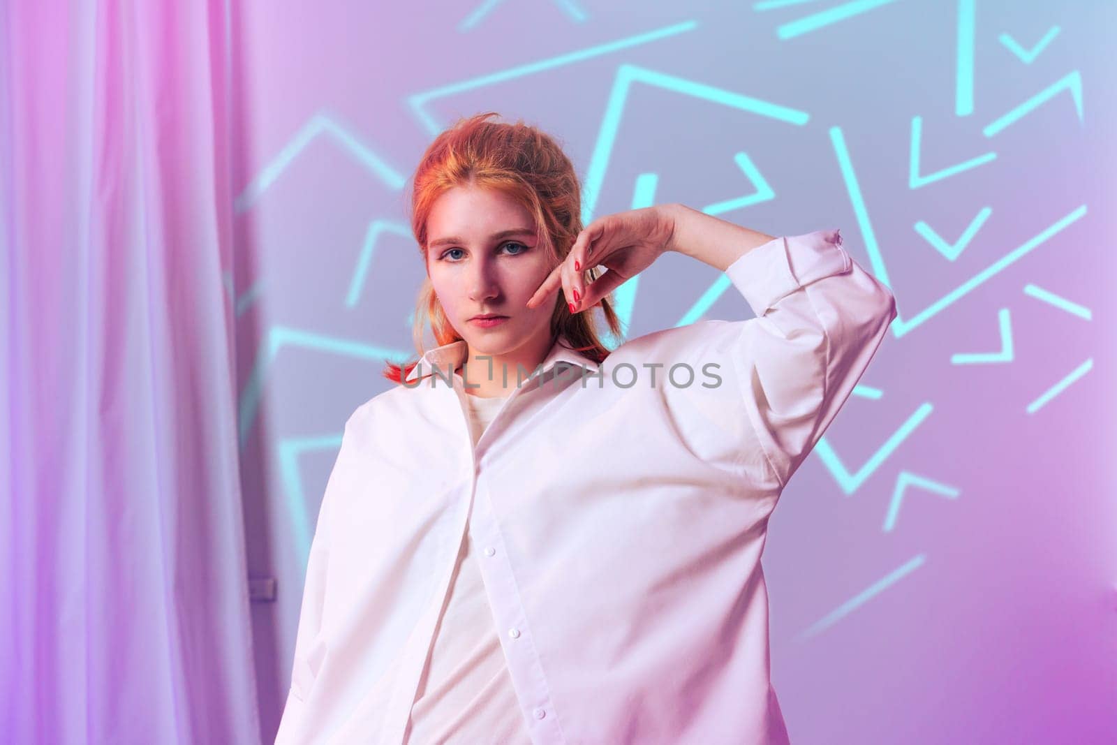 A young woman stands with one hand raised, wearing an oversized white shirt.