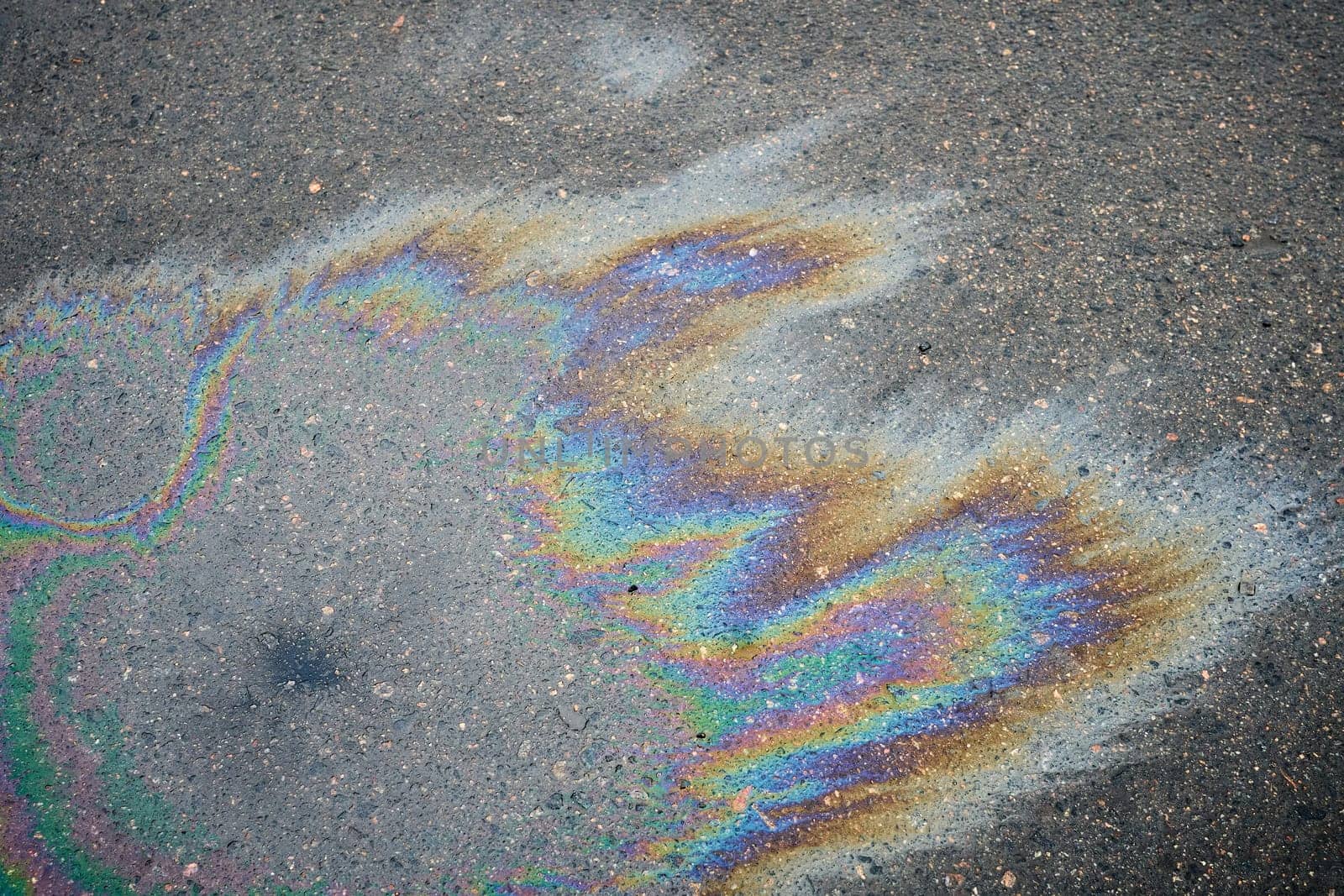 Iridescent oil spill forms vibrant rainbow patterns on rough asphalt surface.
