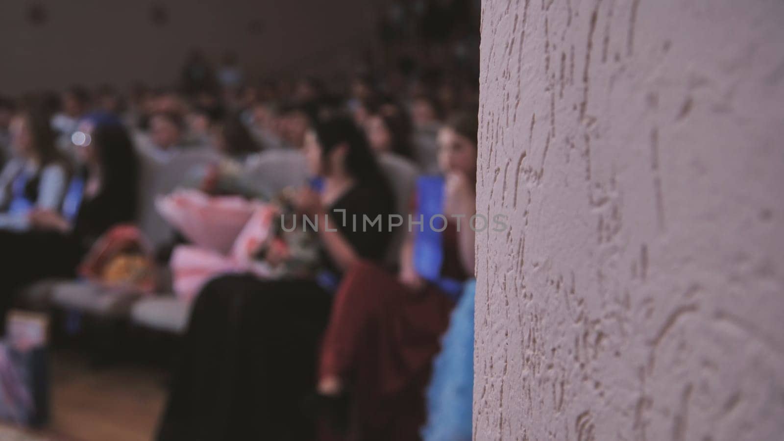 Blurred audience enjoying a graduation ceremony, with a textured wall providing an intriguing backdrop to the celebration of achievement