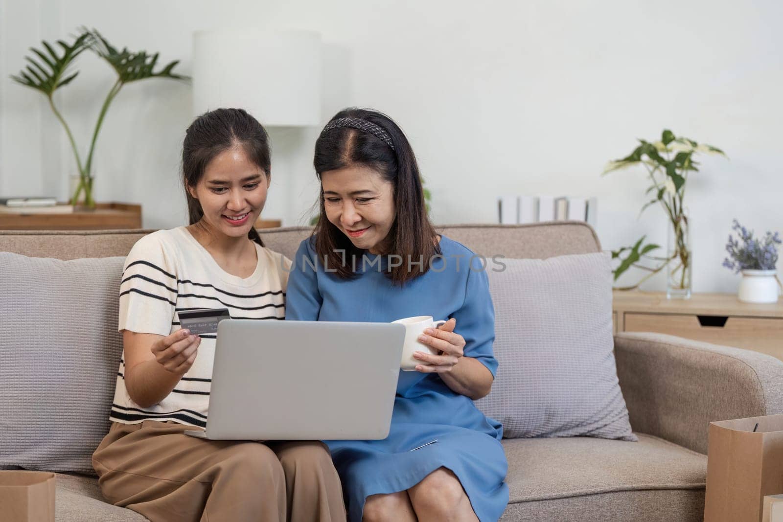 A mother and child happily shop online using a laptop and credit card, enjoying a cozy and modern home setting.
