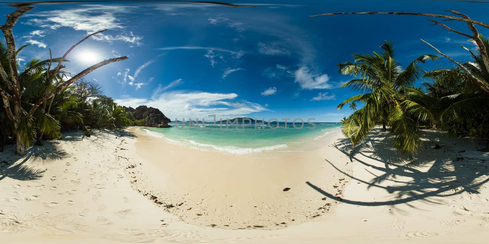 A serene beach lined with swaying palm trees offers cool shade, while gentle waves lap at the pristine shoreline. La Digue, Seychelles. 360 panorama VR.
