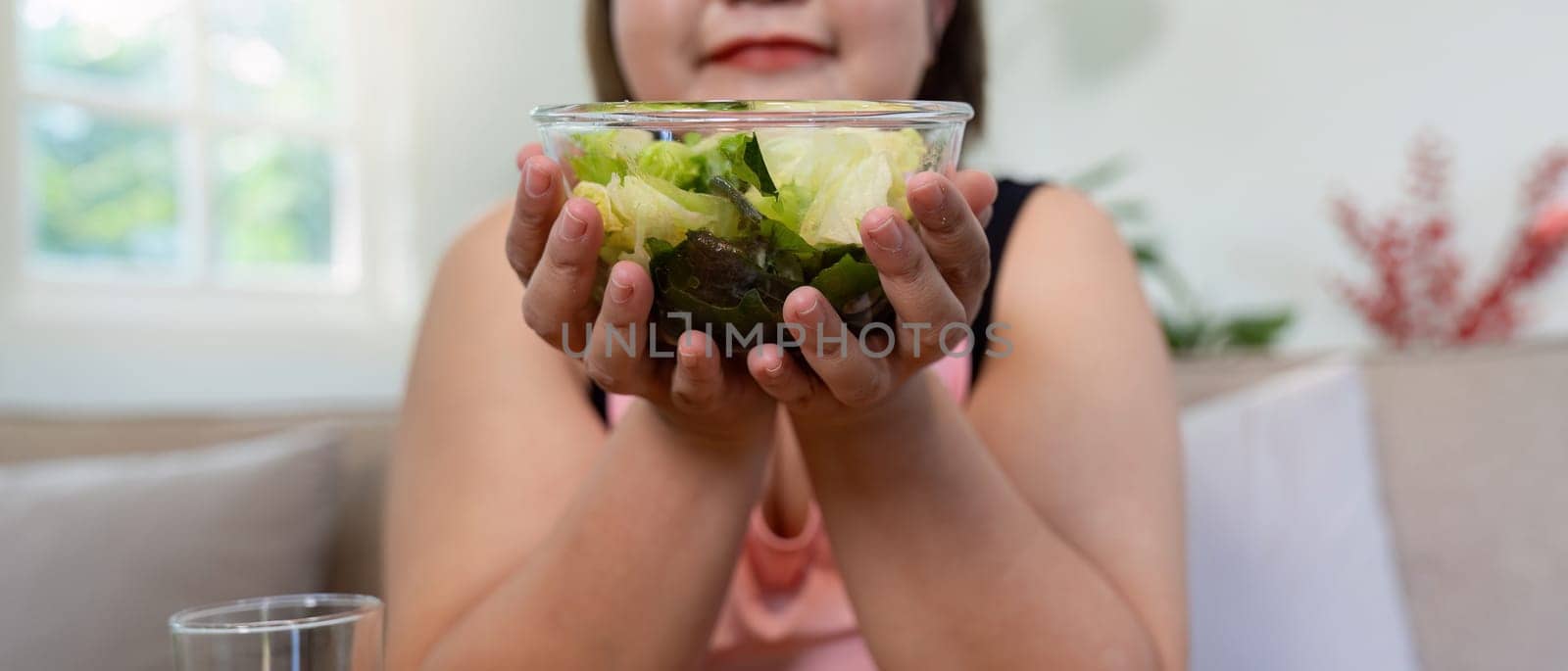 An overweight woman proudly holding a bowl of fresh salad, promoting healthy eating and weight loss in a cozy home atmosphere.