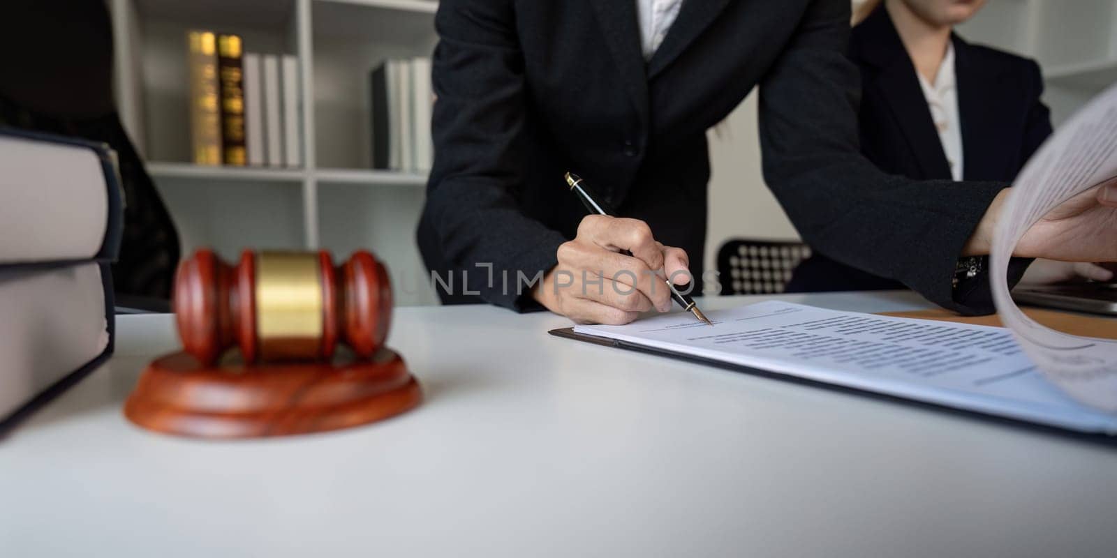 A lawyer carefully signing important legal documents at a desk, with a gavel visible, in a formal office setting.