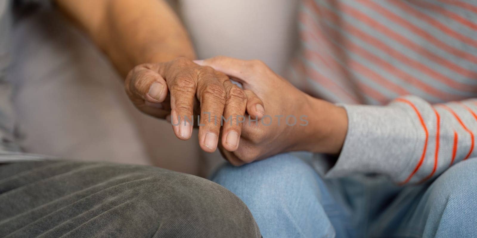 A close-up view of a young man gently holding hands with his elderly father, symbolizing love and connection in their family relationship.