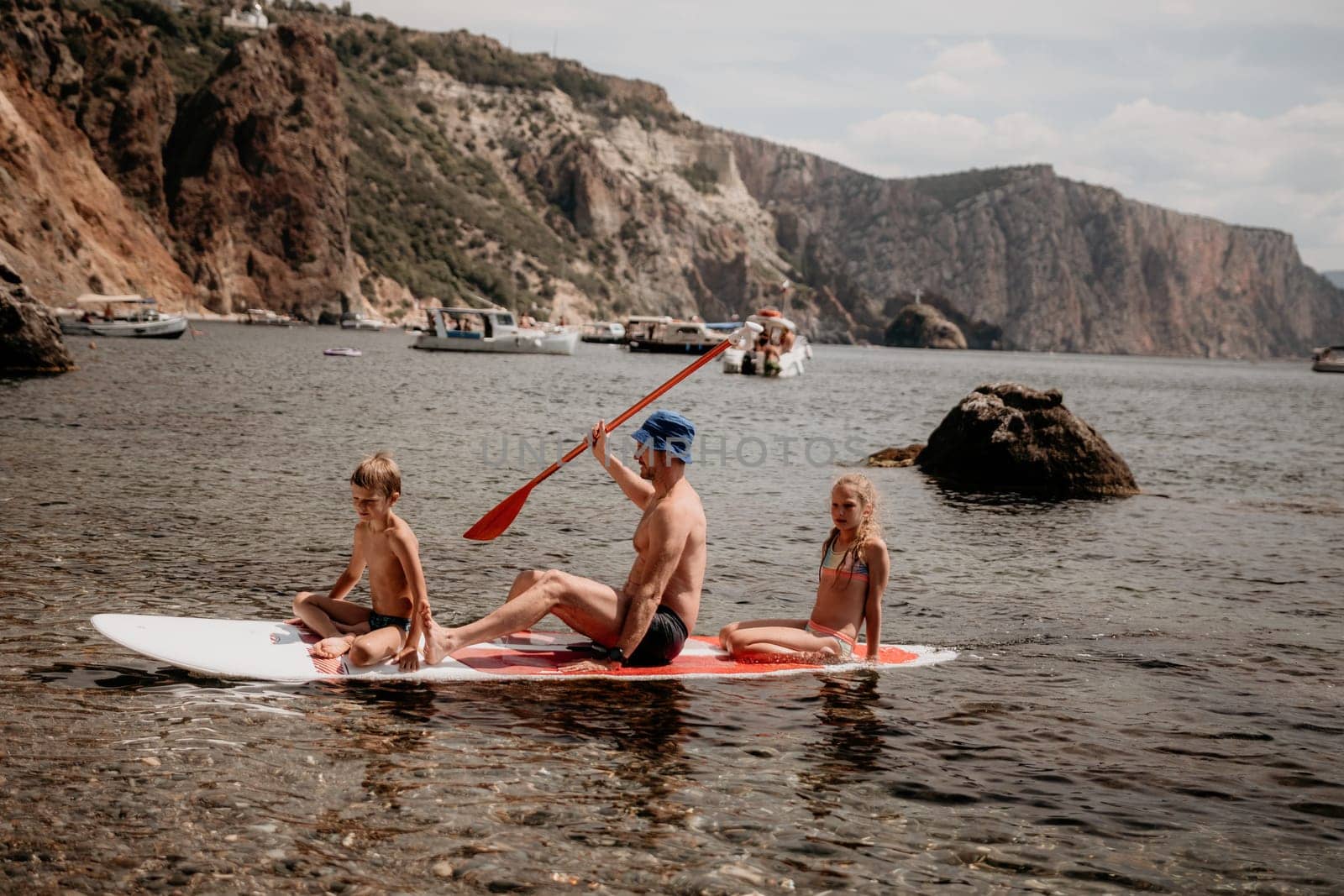 Family sea sup. Young happy father with his son and daughter Floating on a SUP board, paddling in blue sea water. summer vacation and Dad and Son Daughter concept. by panophotograph