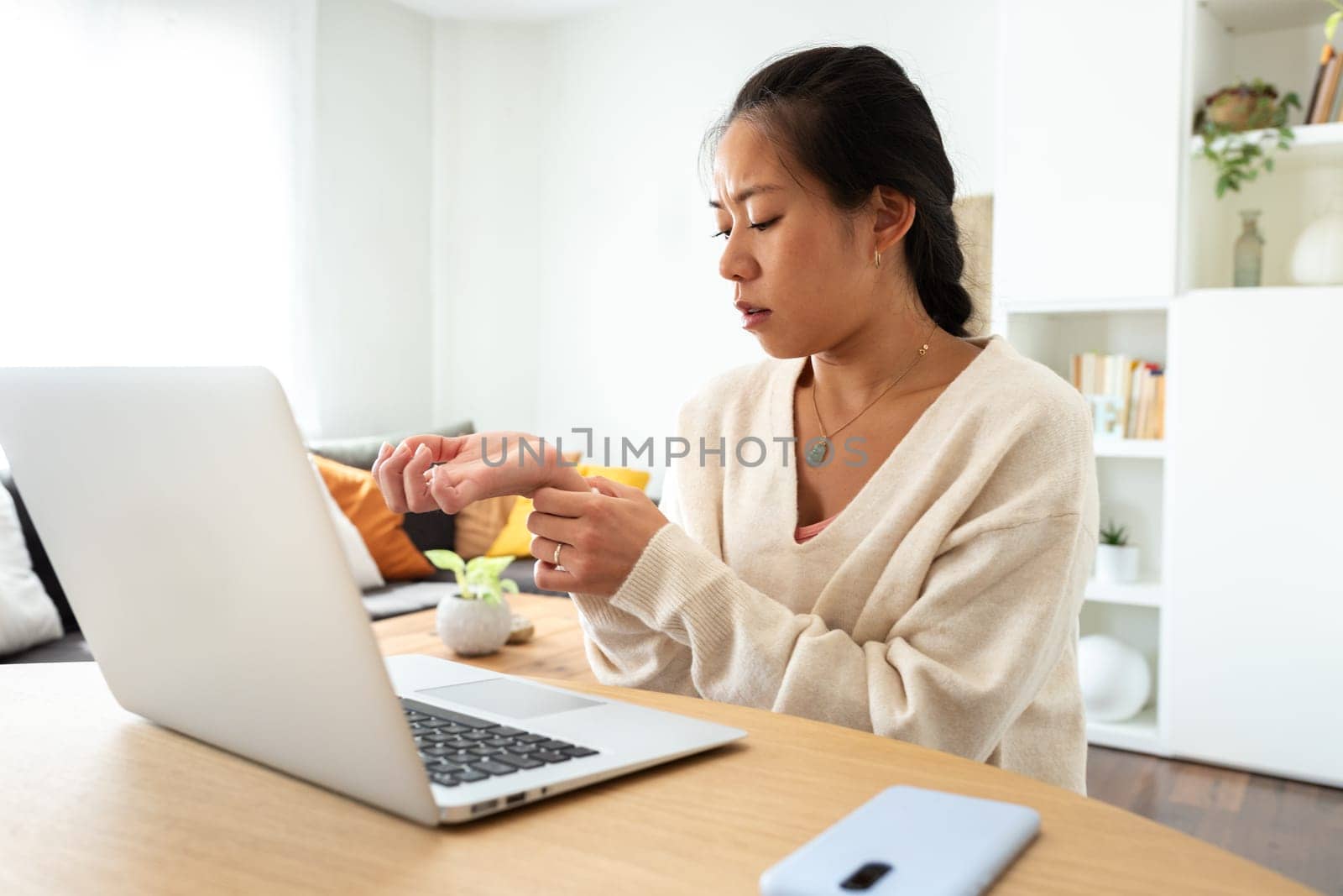Asian woman suffering from wrist pain from working with laptop at home office. Body care concept.