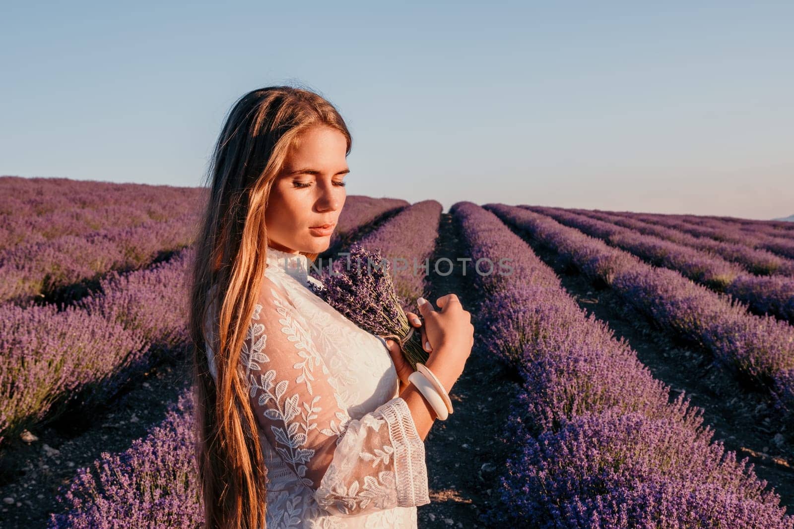 Woman lavender field. Happy carefree woman in a white dress walking in a lavender field and smelling a lavender bouquet on sunset. Ideal for warm and inspirational concepts in wanderlust and travel. by panophotograph