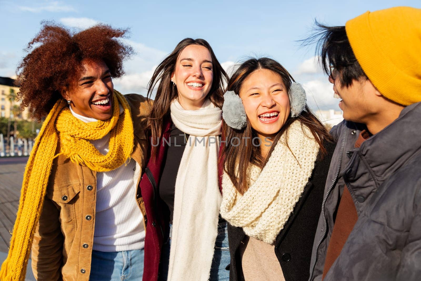 Happy chinese young woman enjoying sunny winter day with multi-ethnic diverse group of friends. People embracing having fun laughing outdoors. Lifestyle concept.