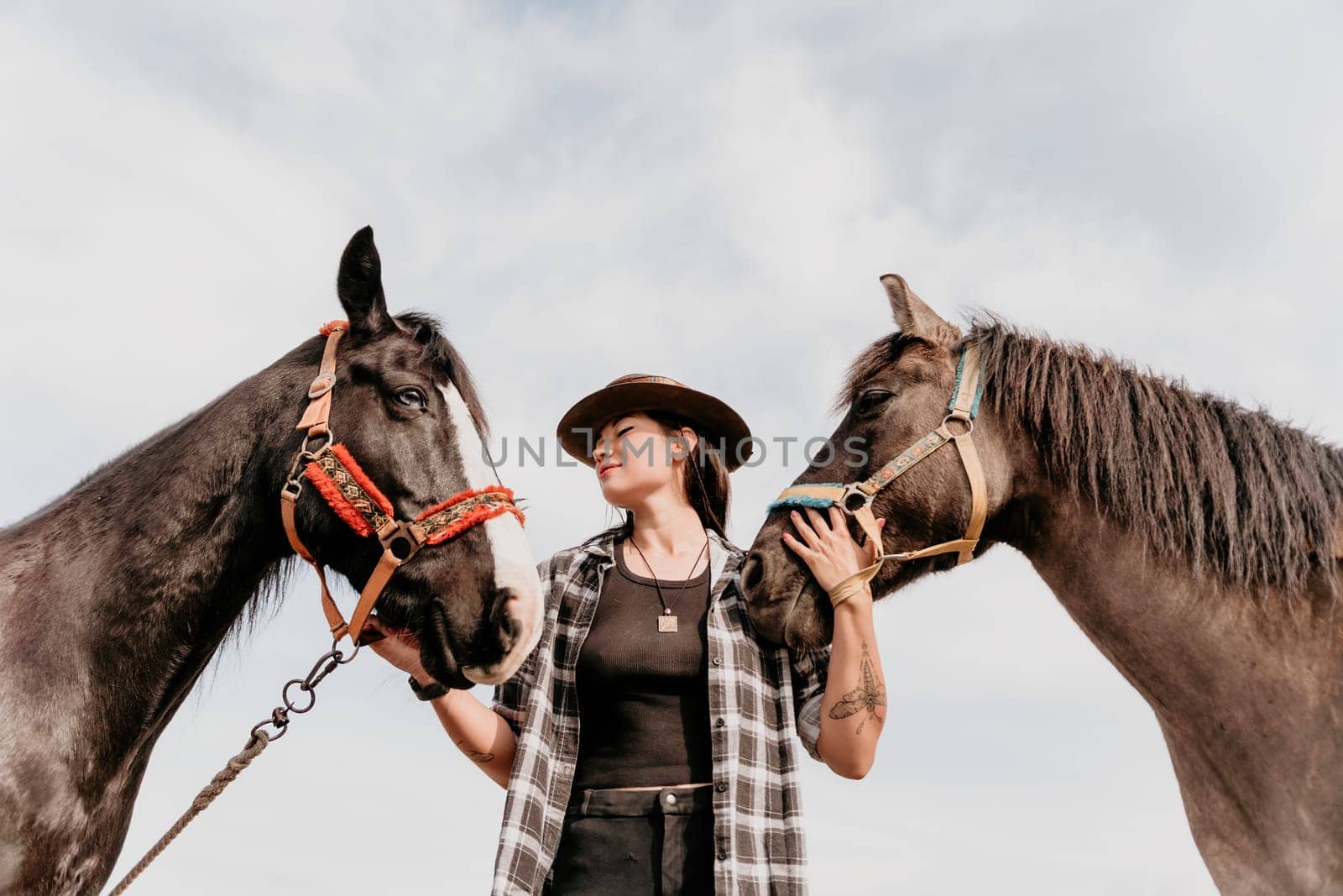 Young happy woman in hat with her horse in evening sunset light. Outdoor photography with fashion model girl. Lifestyle mood. Concept of outdoor riding, sports and recreation. by panophotograph