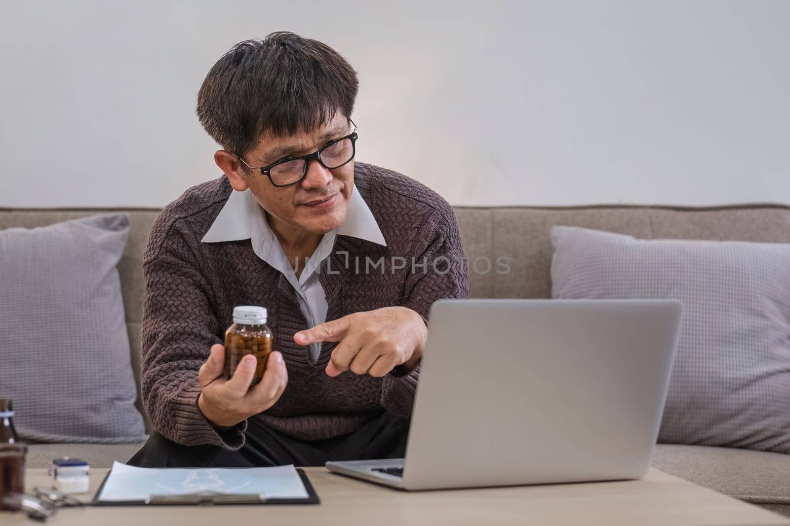 A curious elderly man holds a medicine bottle. Consult with doctor about medication use via video call. Talk to doctor..