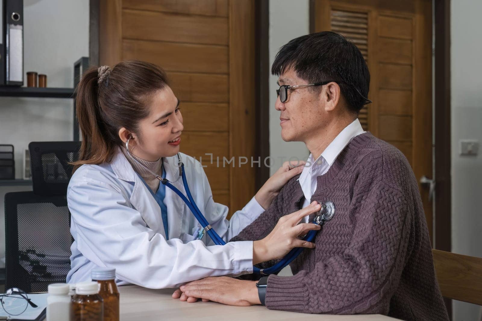 The female doctor in charge holds a stethoscope and listens to the patient. Doctor checking heartbeat examining retired elderly man at home Senior heart disease, health checkup concept health care by wichayada