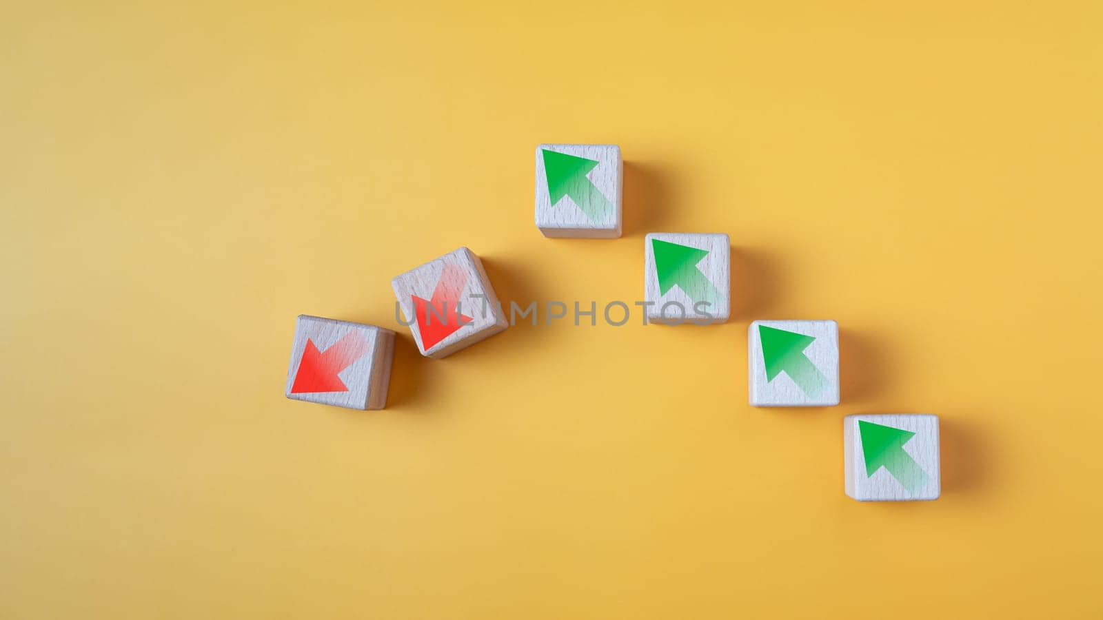 Green arrow and red arrow on wooden block represents economy trending downwards on yellow background. Economy recession crisis, inflation, stagflation, business and financial loss concept. by Unimages2527