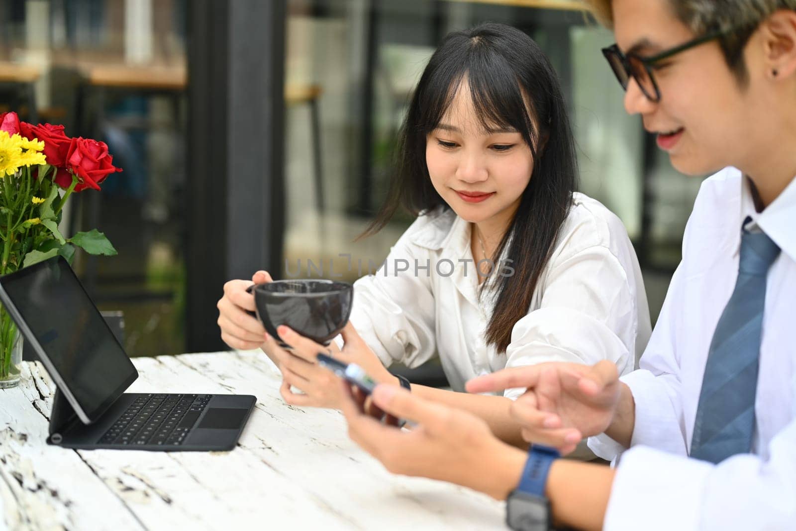 Image of young corporate colleagues talking and watching social media content on mobile phone during break by prathanchorruangsak