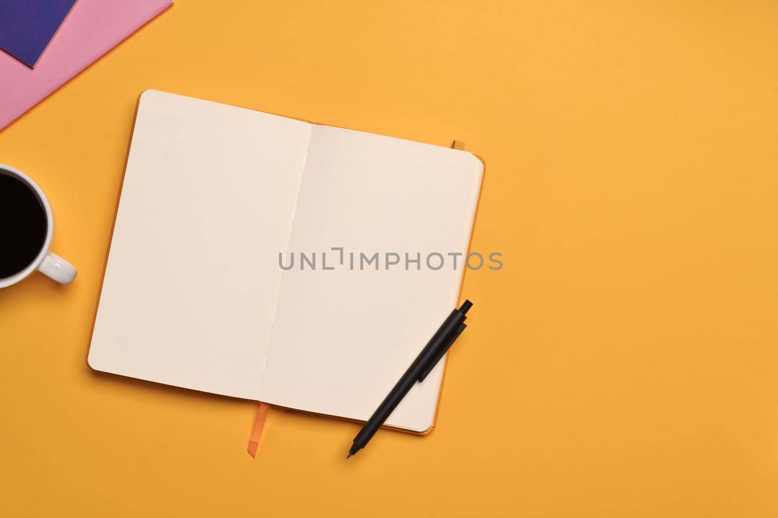 Blank open notebook, pen and cup of coffee on yellow background. Top view with space for text.