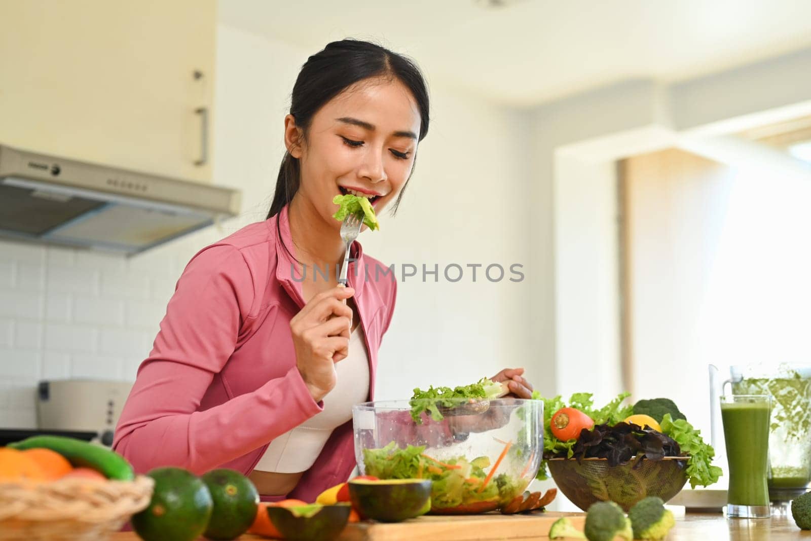 Attractive young woman eating healthy vegetable salad in kitchen. Healthy lifestyle concept.