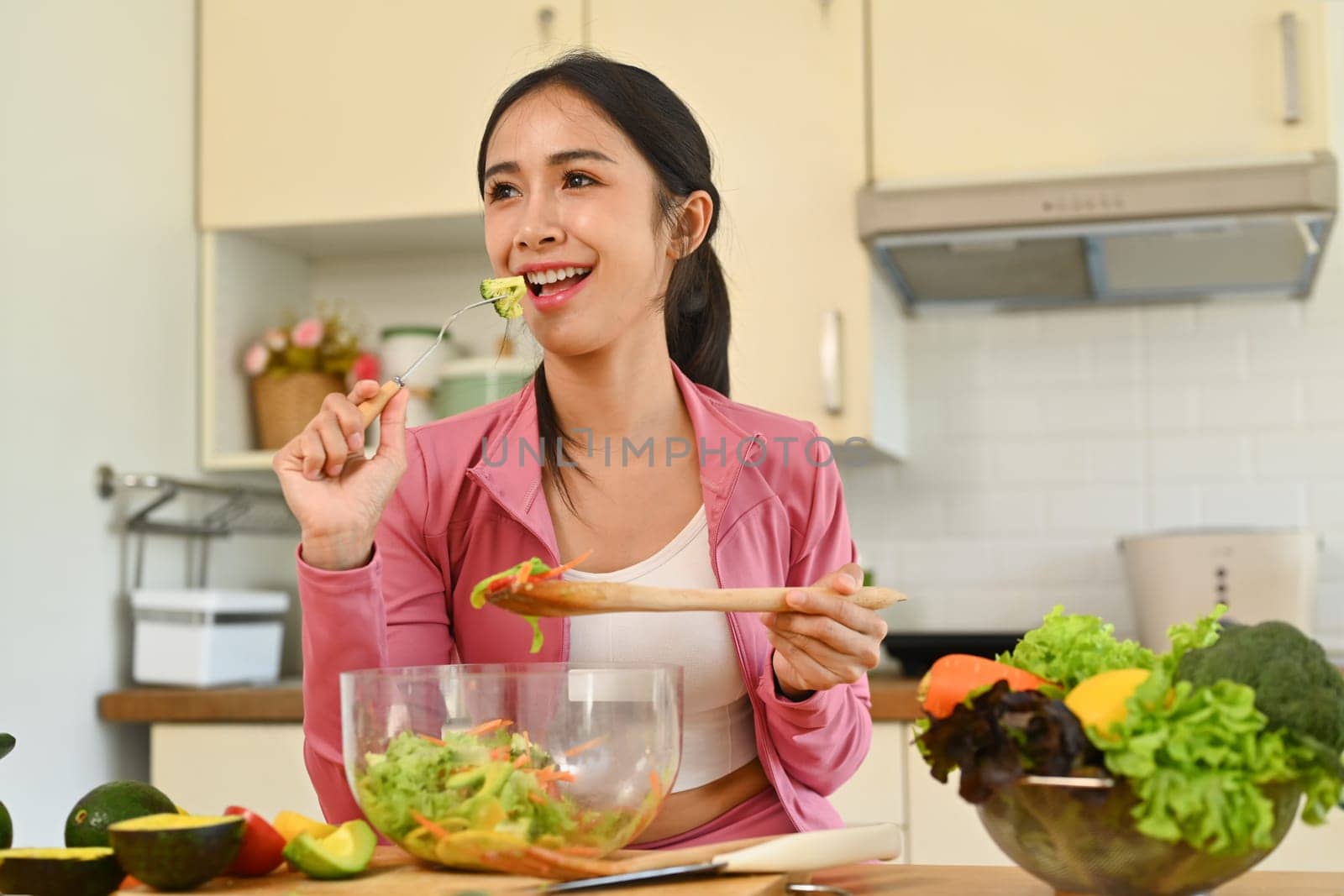 Portrait sporty woman eating vegetable salad in the kitchen. Dieting, health lifestyle and nutrition concept.