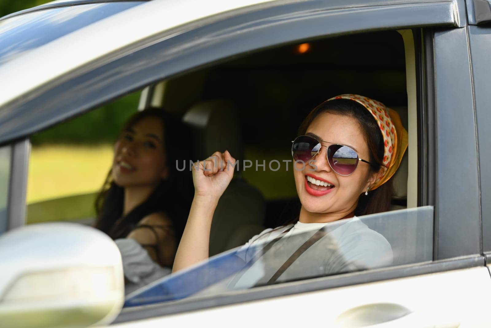 Cheerful female friends singing and dancing in car on road trip, enjoy holidays together by prathanchorruangsak