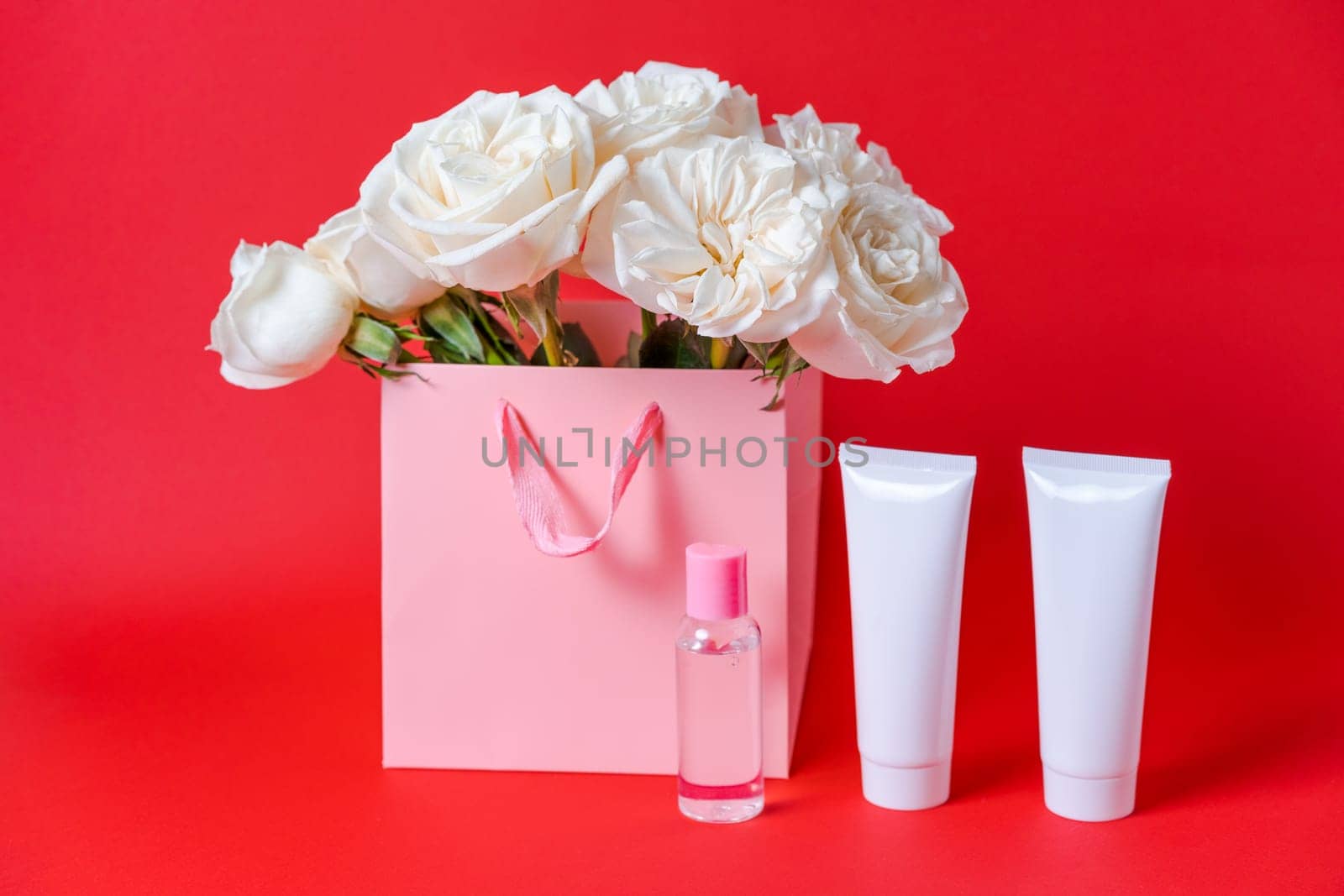 Bouquet white roses and cosmetic white tube for face cream, cleanser or body lotion on red. Moisturizing cosmetic product concept mockup