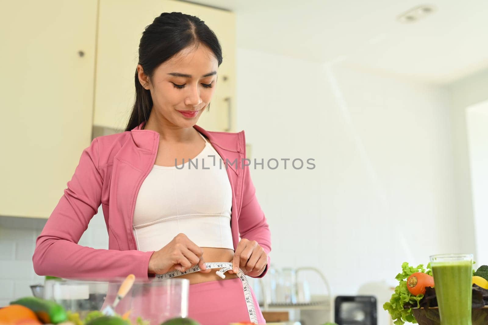 Satisfied young woman measuring waist with tape. Dieting, weight loss and healthy lifestyle concept by prathanchorruangsak