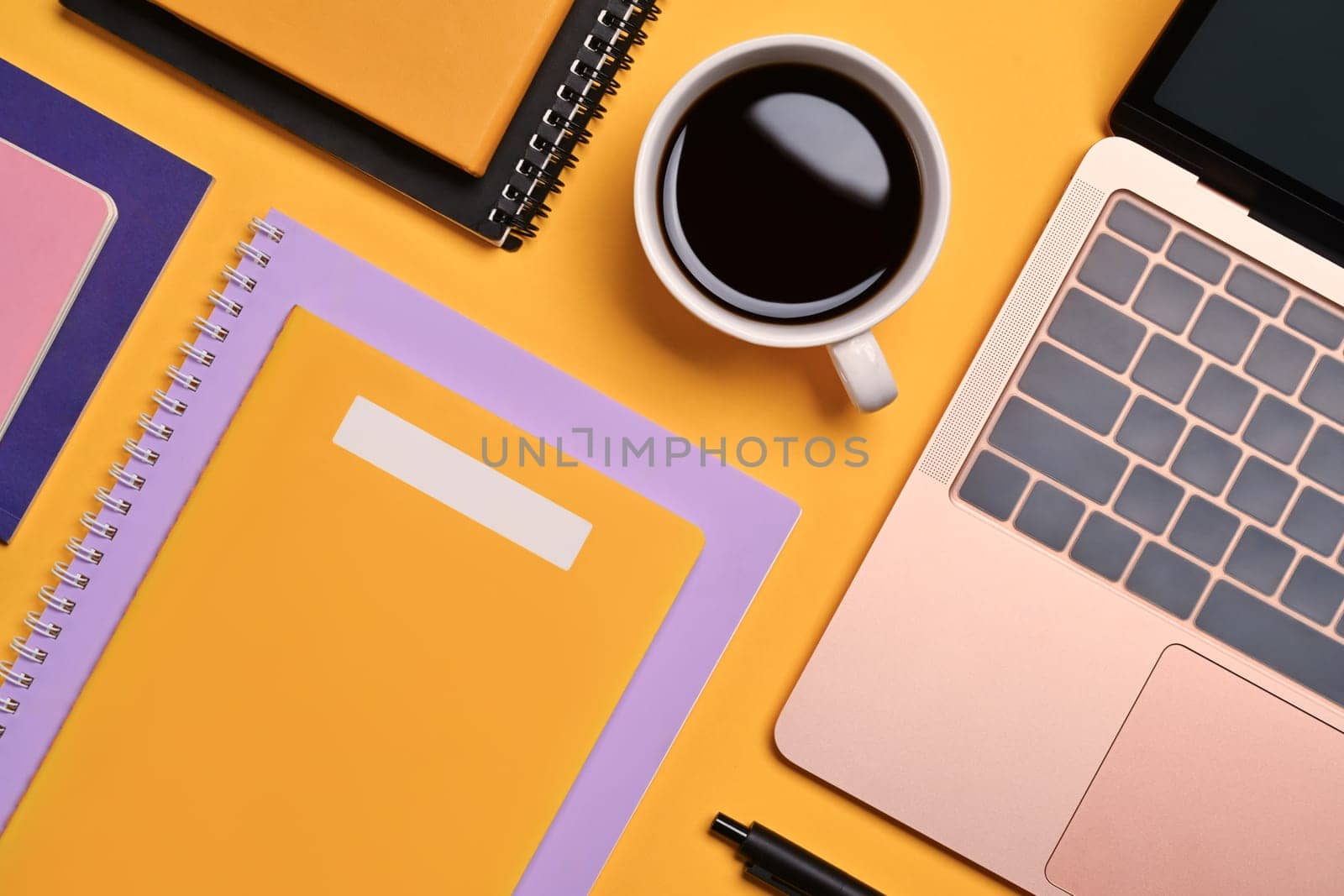 Top view laptop, cup of coffee and notebooks on yellow background.