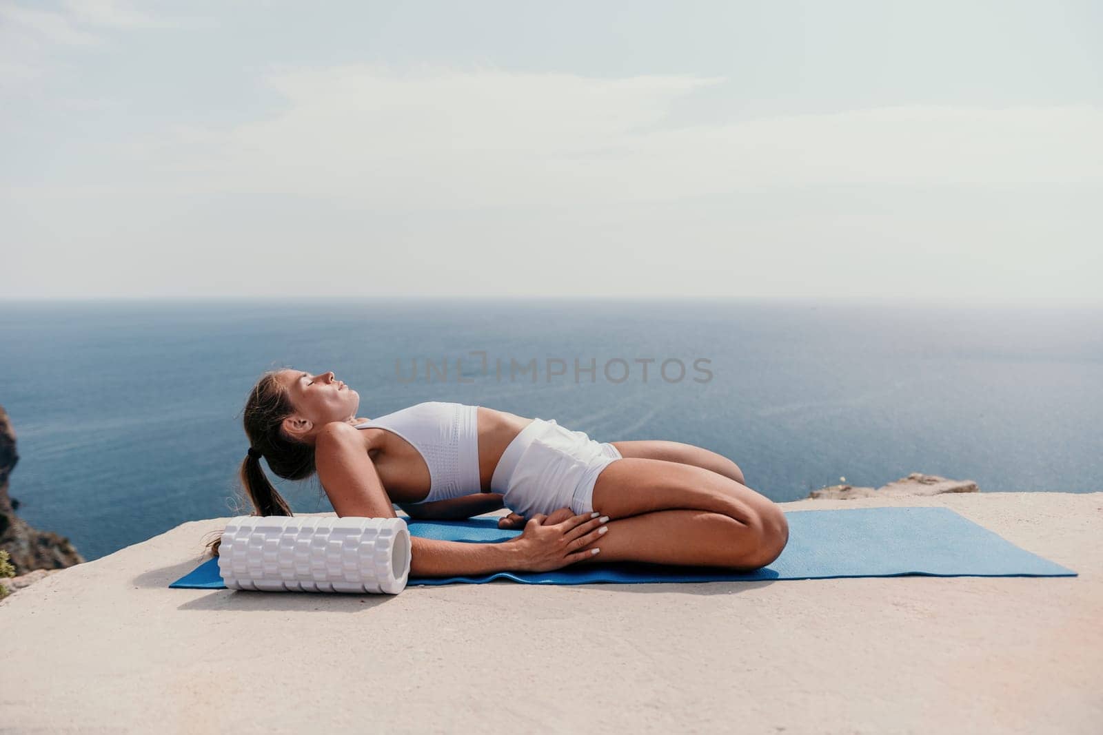 Middle aged well looking woman with black hair doing Pilates with the ring on the yoga mat near the sea on the pebble beach. Female fitness yoga concept. Healthy lifestyle, harmony and meditation.