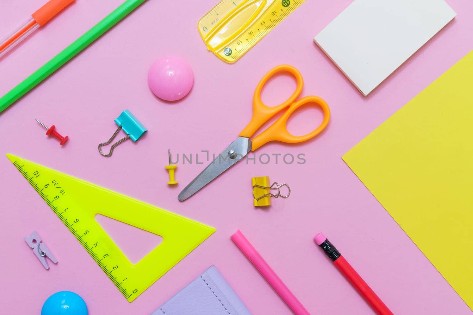 White notepad on spring and stationery school supplies on a pink background, heaps of colored pencils, paper clips, multi-colored objects for work and creativity, back to school